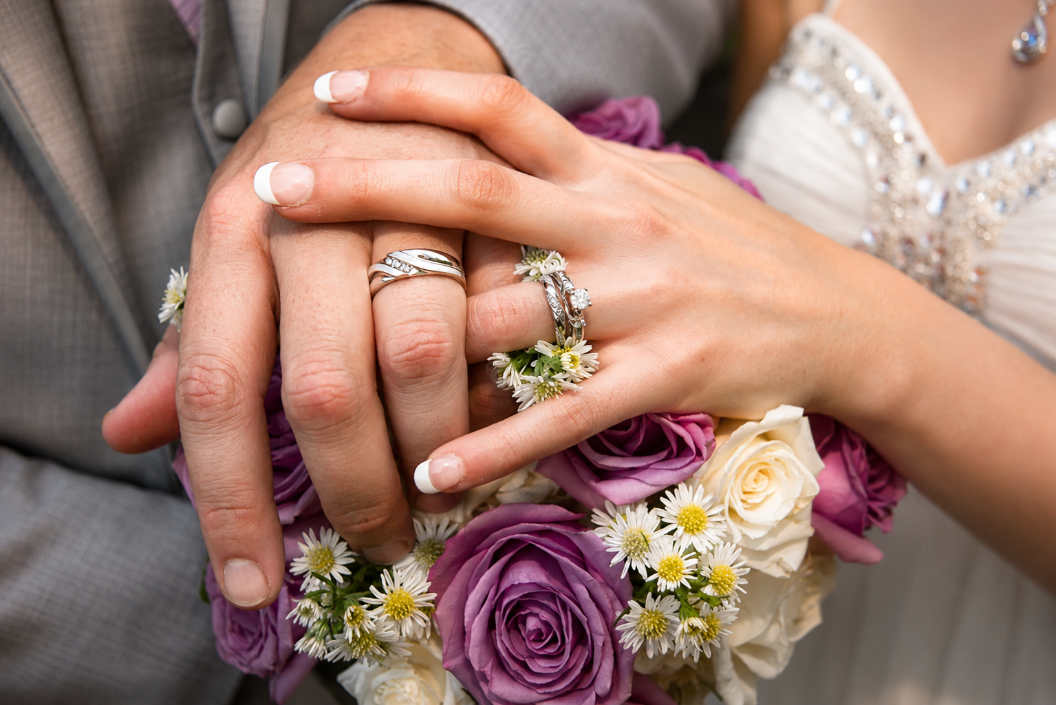 Wedding rings and bouquet detail with purple and white roses