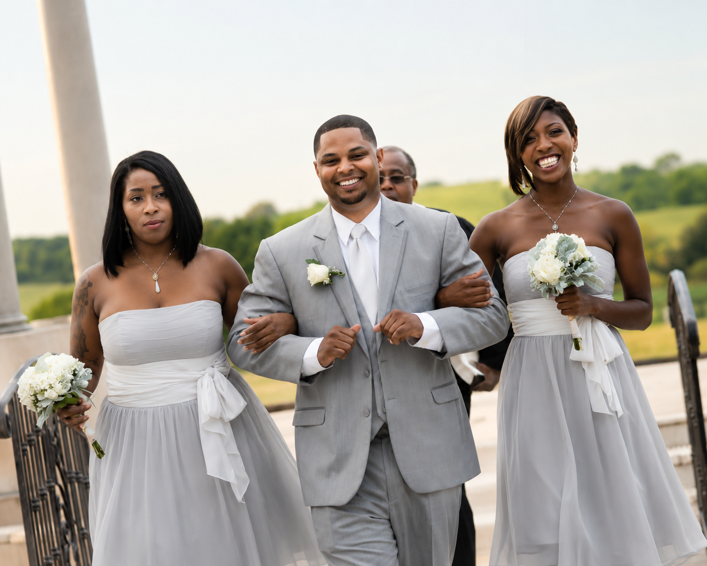 Groom escorted by bridesmaids in silver gowns at outdoor ceremony