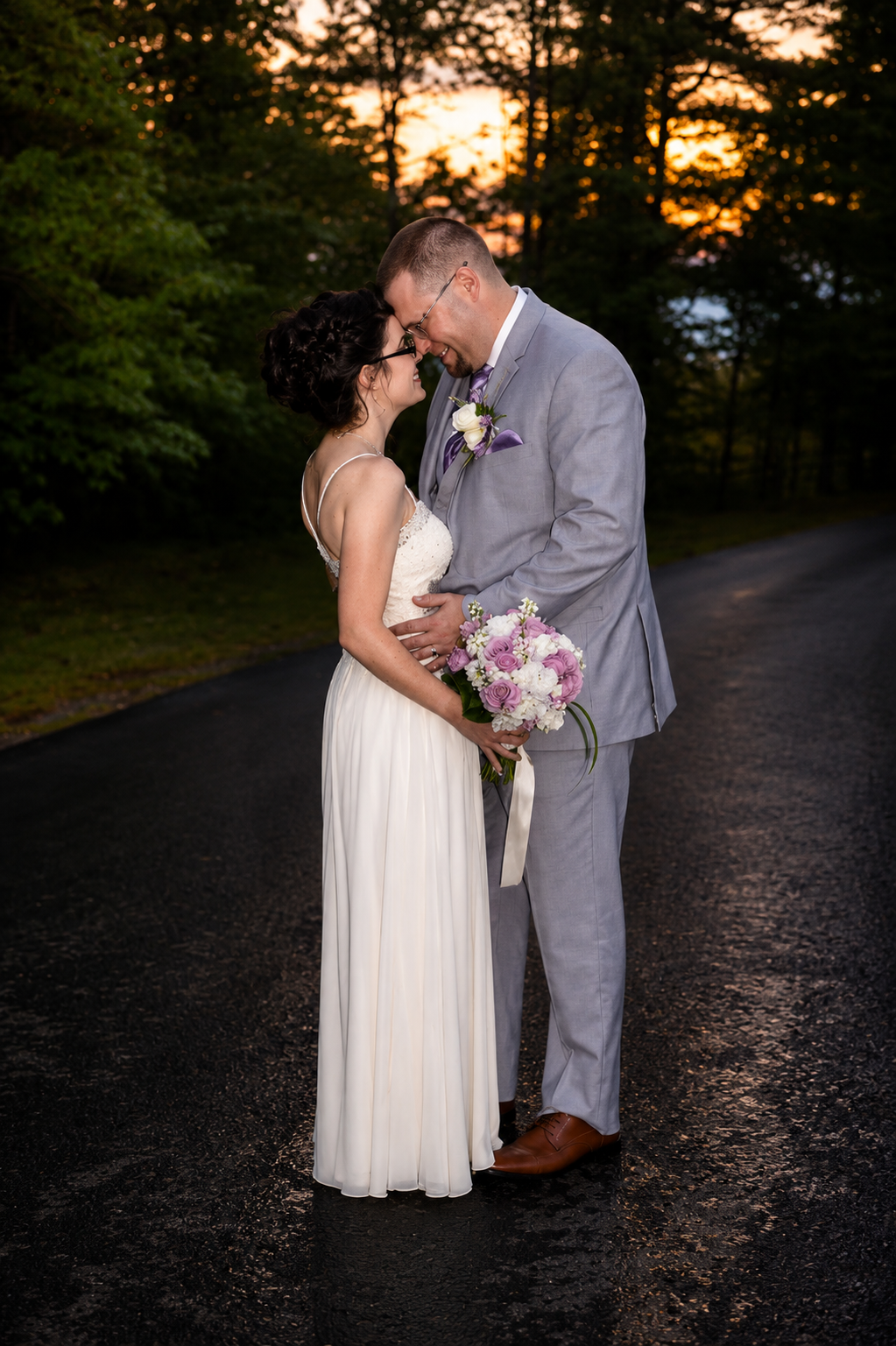 Bride and groom sharing a romantic moment at sunset on a wooded road
