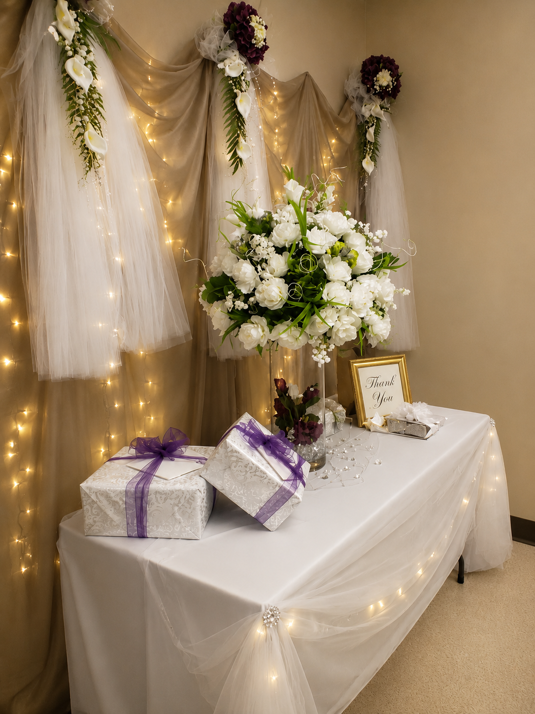 Wedding gift table with white floral arrangement, purple ribbon gift boxes and fairy light tulle backdrop