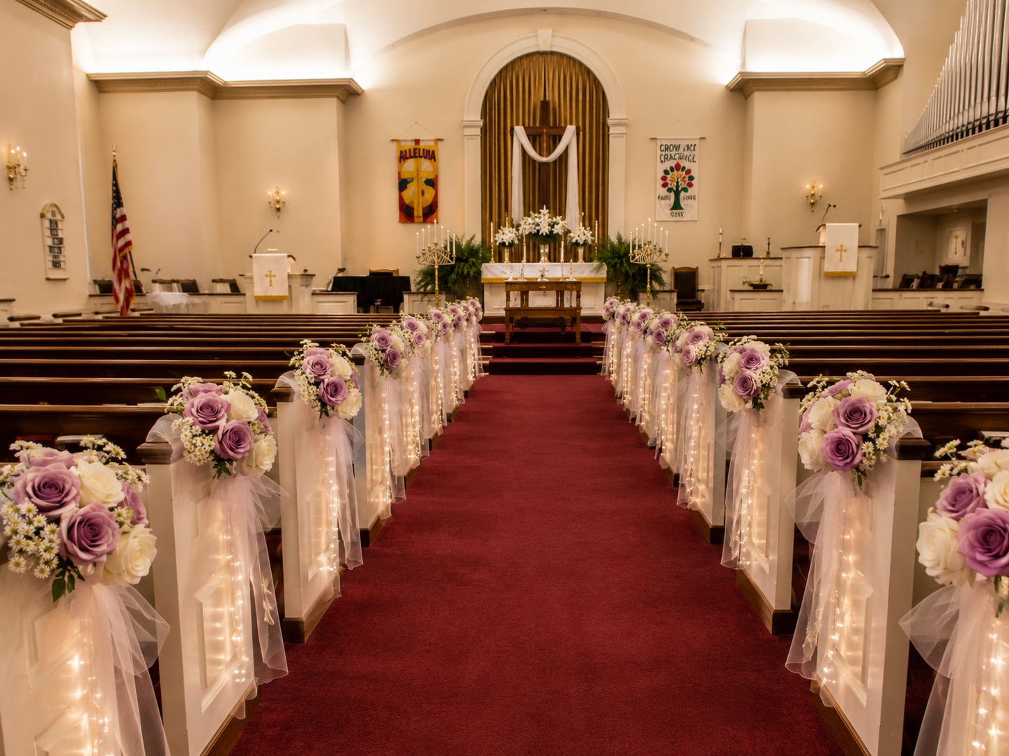 Church aisle decorated with lavender and white rose pew arrangements, tulle and fairy lights leading to the altar
